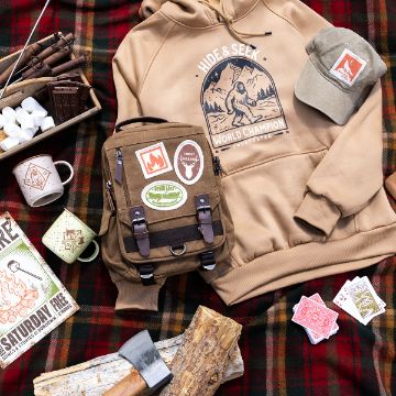 Show details for Square Blank Finished Edge Patches (4-Pack) Camping-themed items on a plaid blanket: a tan hoodie, matching hat, brown backpack with patches, mugs, playing cards, firewood, marshmallows, snack bars, and a campfire booklet. All feature outdoors or Bigfoot motifs.