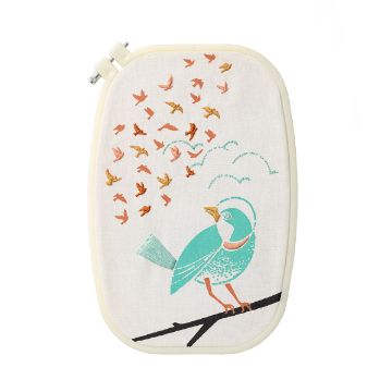 Show details for Birds Flying High Embroidery Floss & Needle An embroidery hoop holds fabric with a stitched design of a turquoise bird sitting on a branch, looking up at a flock of smaller orange and teal birds flying above.