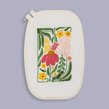 Show details for Linen (White, 17½" x 21¼”) An embroidery hoop displays a colorful floral design with pink, yellow, and red flowers, green leaves, and a butterfly on white fabric, set against a light purple background.