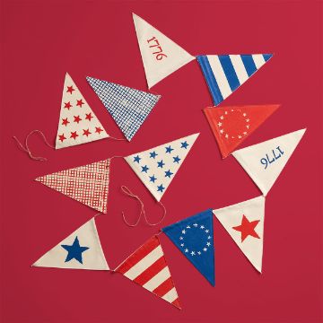 Show details for Fabric Pennant Banner A set of patriotic triangular pennant flags in red, white, and blue patterns, including stars, stripes, checks, and the years "1776" and "9111," arranged on a red background with twine.