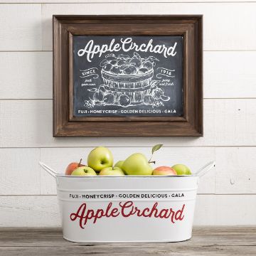 Show details for Apple Orchard Encore A white metal tub labeled "Apple Orchard" holds green and red apples beneath a framed chalkboard sign with a drawing of apples and the words "Apple Orchard" on a white wall.