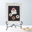 A framed blackboard on a stand displays three donut-shaped magnets and a note reading "DONUT WORRY!" Nearby, a plate holds three sprinkled donuts on a white table with a light blue background.