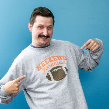 Show details for Weekend Forecast A smiling man with a mustache points at his gray sweatshirt, which has an illustration of a football and the text "Weekend Forecast" printed on it. He stands in front of a solid blue background.