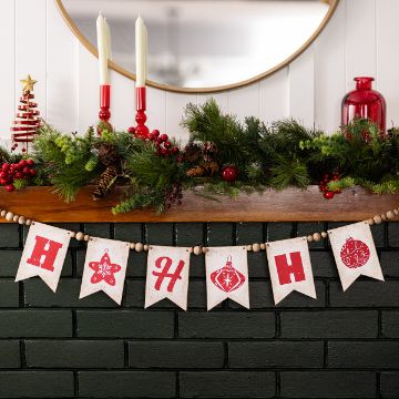 Show details for Ho Ho Ornaments A festive mantel decorated with greenery, red berries, pine cones, candles, and holiday ornaments. A banner with red letters and holiday symbols spells out “HO HO HO” across the front.