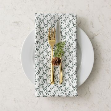 Show details for Ho Ho Pattern A white plate with a gold fork and knife placed on a white napkin with “ho ho ho” script. A small pine branch and pine cone rest above the cutlery, creating a festive holiday table setting.
