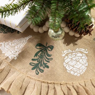 Show details for Elegant Holiday Icons Close-up of a festive burlap tree skirt with printed designs of a tree, mistletoe, and pinecone, bordered by ruffles. A pine branch, pinecones, white beads, and wrapped gifts are partially visible at the top.