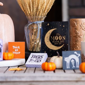 Show details for Chubby Square (3-Pack, 3" x 3") A Halloween-themed display features small pumpkins, festive signs reading "Trick or Treat," "Hocus Pocus," and "The Moon Made Me Do It," a purple candle, wheat in a glass vase, and a pumpkin-shaped decor item.