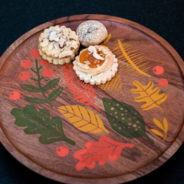 Show details for Leaf It To Me A wooden tray decorated with colorful leaves and berries holds three cookies: one with almond slices, one with an apricot center, and one dusted with powdered sugar.
