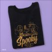 A black t-shirt folded neatly on a purple surface, featuring gold line art of Peanuts characters and the text “Spooky Crew” with “Good Grief!” written below.