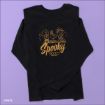 A black long-sleeve shirt featuring orange "Spooky Crew" text and Peanuts characters with pumpkins on the front, laid flat on a light purple background.