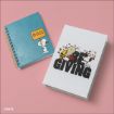 Two Peanuts-themed notebooks on a pink surface: one blue spiral notebook with Snoopy holding a "BOO!" sign, and one white hardcover notebook with Snoopy and Charlie Brown and the text "GIVING.