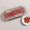 A vintage-style sign reads "Fresh Strawberries 25¢/Pint" next to a small white bowl filled with fresh strawberries, placed on a light-colored surface.