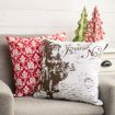 Two decorative pillows on a gray chair; one is red with a white damask pattern, the other is white with a vintage Santa Claus and "Joyeux Noël" inscription. Two festive tree ornaments are in the background.
