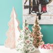 Three decorative paper Christmas trees with different patterns stand on a white surface; one has holly and berries, another has a pink damask design, and a bowl of striped peppermints sits nearby. A festive painting hangs on the wall behind them.