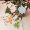 Christmas ornaments, including two green trees, a blue mitten, two red-and-white candy canes, and a gingerbread person, are displayed on and beside a small decorated pine branch.