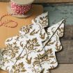 A spool of red and white twine sits next to folded, patterned paper cut-outs shaped like Christmas trees with gold floral designs on a rustic wooden surface.