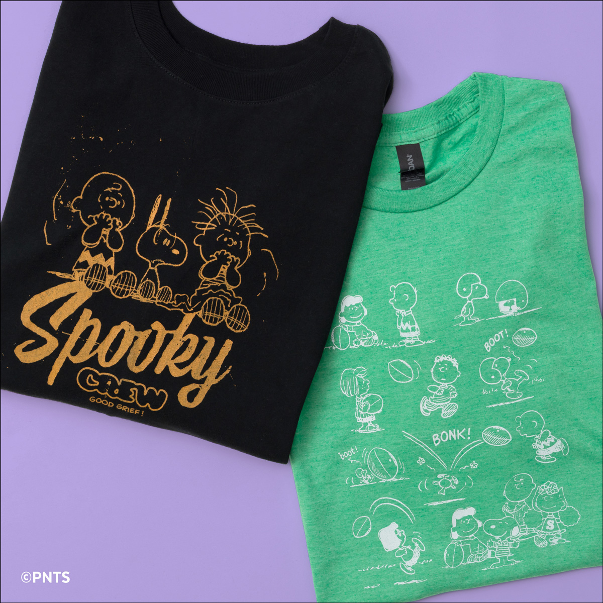 Two folded Peanuts-themed T-shirts on a lavender background: one black with "Spooky" and gold outlines of Charlie Brown characters; one green featuring white cartoon scenes of Peanuts characters playing football.