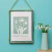A framed illustration of snowdrop flowers labeled "January Snowdrop" hangs on a turquoise wall next to a matching vase holding real snowdrops.