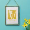 A framed artwork of a yellow daffodil with the text "MARCH Daffodil" hangs on a turquoise wall. A small bouquet of real daffodils is placed nearby.
