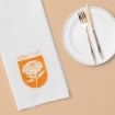 A white napkin with an orange marigold illustration and the text "October Marigold" next to a white plate with a gold knife and fork, all on a beige surface.