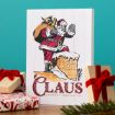 A festive card featuring Santa Claus carrying a sack and stepping into a chimney, with the text “Claus Chimney Service Co.” Below, there are wrapped gifts with red ribbons and spruce branches on a wooden surface.