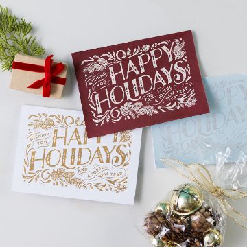 Show details for Happy Holidays A small gift box, festive pine branch, and bag of gold jingle bells sit beside three "Happy Holidays and a Joyful New Year" greeting cards in red, gold, and silver on a light background.