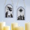 Two stained glass-style ornaments with nativity silhouettes hang above lit candles. One shows an angel with Mary, Joseph, and baby Jesus; the other features the three wise men following a star.
