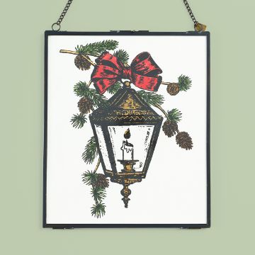 Show details for Winter Lantern Framed illustration of a vintage lantern with a lit candle inside, decorated with pine branches, pinecones, and a red bow. The frame hangs from a chain against a light green background.