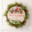 A festive wreath with pine branches, red berries, and green leaves surrounds a round sign reading “Merry Christmas & Happy New Year” with two red cardinals and pinecones, hanging on a white door.