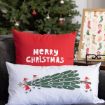 Two festive pillows on a couch; one red with the words "Merry Christmas," and one white with an illustration of Santa decorating a tree. A Christmas tree and framed holiday-themed print are in the background.
