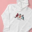A white hoodie on a pink background features an illustration of three birds wearing winter accessories, sitting on a branch, with the text "Winter is for the birds" printed below them.