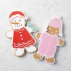 Two decorated cookies on a white surface: one shaped like a snowman with a red hat and dress, the other a gingerbread person in a pink winter hat and onesie, both with smiling faces.