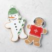 Two decorated cookies on a white surface: one shaped like a snowman with a green hat and a candy cane, the other a gingerbread person in a red sweater with headphones.
