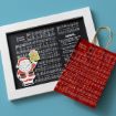 A framed sheet of Christmas music titled "Santa Claus" sits next to a red gift bag with the same sheet music design. A cute cutout of Santa holding a gift is attached to the frame, all on a blue background.