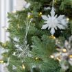 Close-up of a Christmas tree decorated with white and clear snowflake ornaments and small warm white string lights among green pine branches.