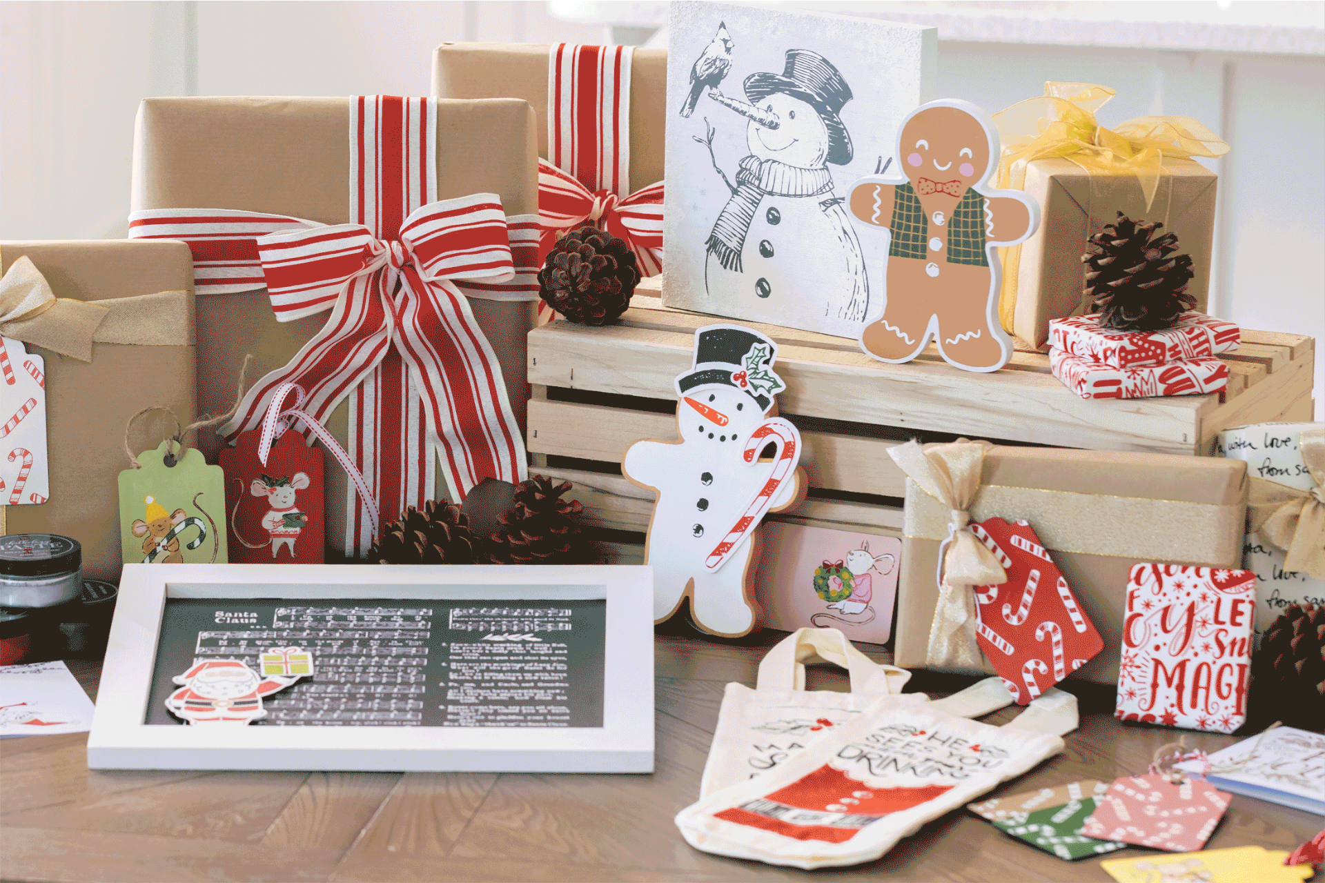 A festive display featuring wrapped gifts with red and white ribbons, gingerbread and snowman decorations, pinecones, holiday tags, and seasonal artwork arranged on a wooden crate and table.