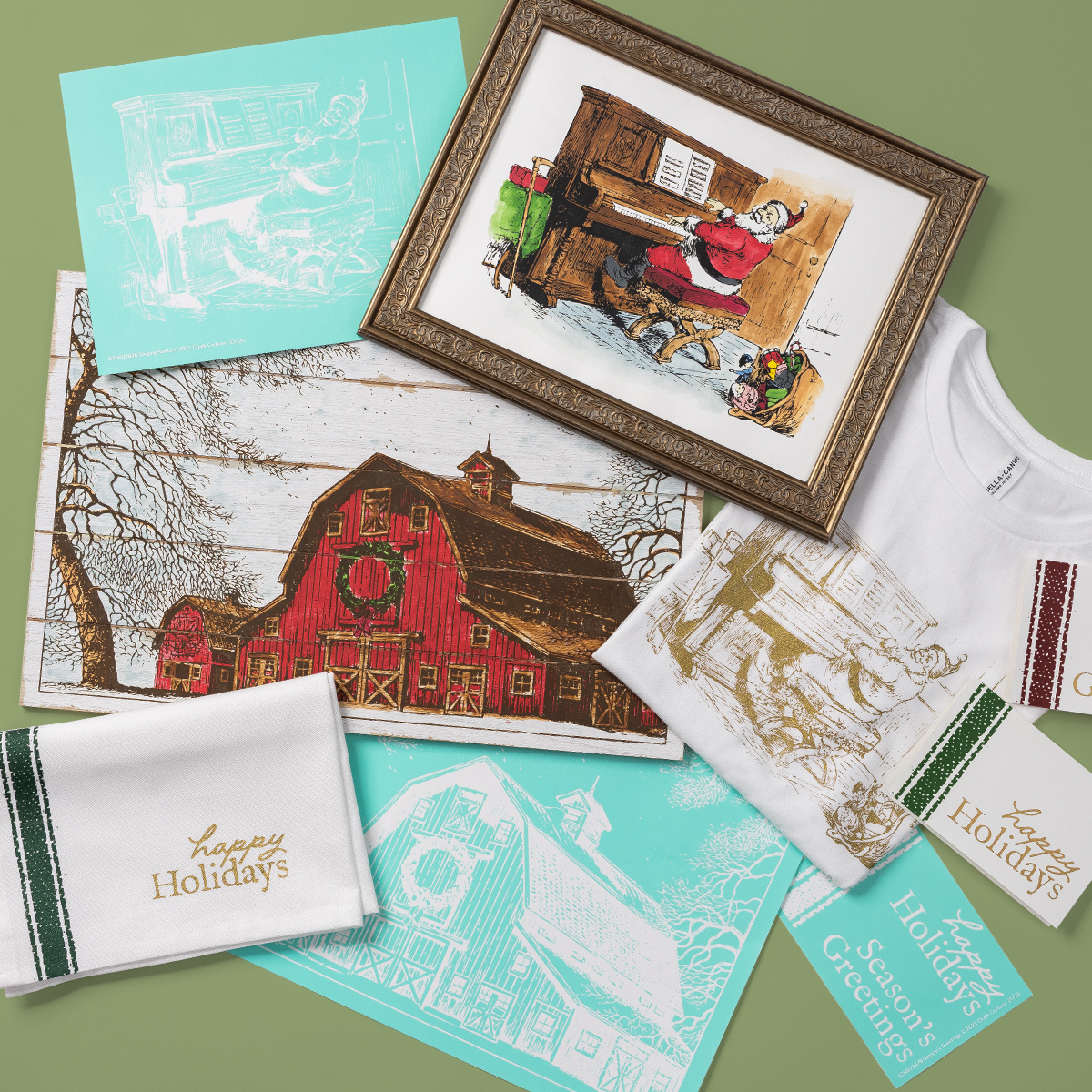 A flat lay of holiday-themed items, including illustrated prints of barns and people at a piano, a framed artwork, a white “Happy Holidays” towel, a T-shirt, and a “Season’s Greetings” card, all on a green background.