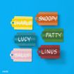 Six colorful name tags on a blue background display the names: CHARLIE (yellow), SNOOPY (orange), LUCY (blue), PATTY (green), SALLY (pink), and LINUS (red).
