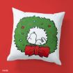 A white pillow features an illustration of Snoopy sleeping curled up inside a Christmas wreath decorated with colorful ornaments and a large red bow, set against a red background.