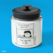 A glass jar with a black lid features a Peanuts comic illustration of Lucy at a booth labeled "PSYCHIATRIC HELP 5¢" and "THE DOCTOR IS IN" on a bright blue background. ©PNTS.
