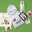 A collection of Peanuts-themed holiday merchandise on a green background, including a hoodie, tote bags, a water bottle, greeting cards, and an e-reader, all featuring Snoopy, Woodstock, and Charlie Brown.