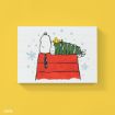 A drawing of Snoopy and Woodstock napping on Snoopy’s red doghouse. Woodstock is wrapped in a green striped scarf. Light blue snowflakes are scattered in the background, all on a yellow backdrop.