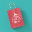 A red paper gift bag with a drawing of a bundled-up animal in a puffy coat and winter hat, set against a teal background. The bag has twisted paper handles and a small copyright mark in the corner.