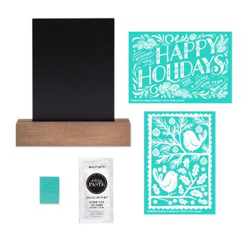 Show details for Happy Holidays Try-Me Kit A chalkboard with a wooden base, two teal holiday stencil sheets, a packet of white paste, and a small teal squeegee, arranged neatly on a white background.