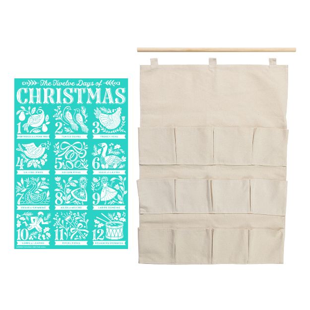 A turquoise "Twelve Days of Christmas" chart with white illustrations is next to a beige fabric wall organizer with twelve pockets and a wooden hanging rod.