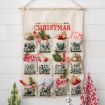 A fabric wall hanging titled "The Twelve Days of Christmas" features twelve numbered pockets, each decorated with festive items like candy canes, ornaments, greenery, a small plush toy, and holiday treats.