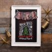 A rustic holiday decor piece with a framed chalkboard sign displaying festive "House Rules," flanked by gold stars, brass bells, and a plaid fabric garland, all set against a wooden background.