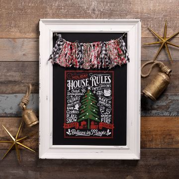 Show details for Debbie - Holiday House Rules A rustic holiday decor piece with a framed chalkboard sign displaying festive "House Rules," flanked by gold stars, brass bells, and a plaid fabric garland, all set against a wooden background.