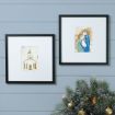 Two framed art prints hang on a light blue wall; one depicts a church, the other shows a stylized Nativity scene. Below, a Christmas tree with gold ornaments is partially visible in the corner.
