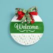A round sign with a green and white design features the word “Welcome” in script. It has a festive bow with red, green, and white plaid and snowflake patterns, set against a light blue background.